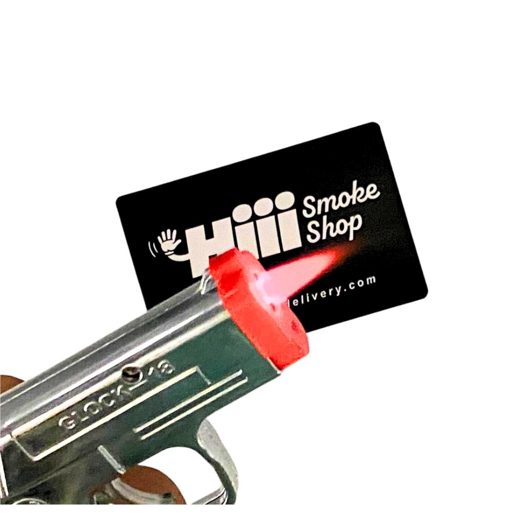 Mini Glock-style torch lighter with red flame tip, featured in front of Hiii Smoke Shop business card – novelty butane lighter for smokers and collectors.