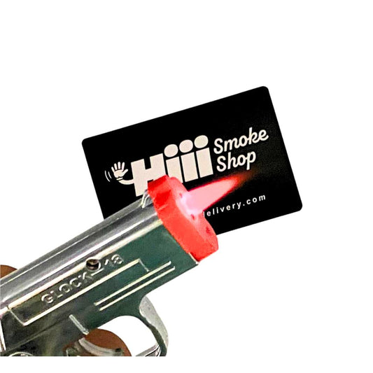 Mini Glock-style torch lighter with red flame tip, featured in front of Hiii Smoke Shop business card – novelty butane lighter for smokers and collectors.